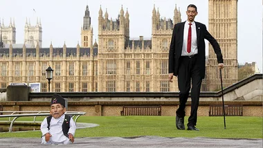 Tallest and shortest men meet in front of the Houses of Parliament, UK; tallest man stands, shortest man sits.
