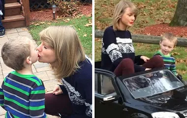 Taylor Swift in festive sweater gives a kiss to a young boy; they sit together in a toy car.