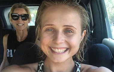 Two women smiling in a car; the front woman is taking the selfie, both look happy.