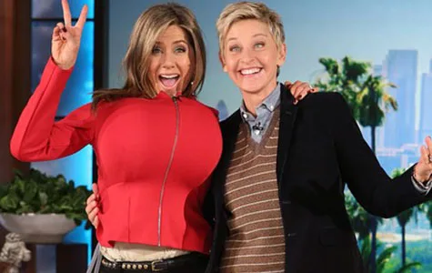 Jennifer Aniston and another person laughing on a TV show set, with Aniston playfully wearing a red jacket.