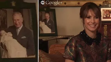 Prince Charles holding baby, framed photo in background, woman smiling in the foreground.