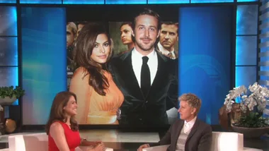 A talk show set with a host and guest discussing an onscreen image of a well-dressed couple at a formal event.