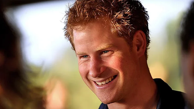 A man with red hair smiling warmly, wearing a dark shirt, with a blurred background.