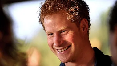 A man with red hair smiling warmly, wearing a dark shirt, with a blurred background.