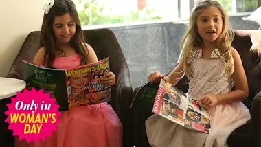 Sophia Grace and Rosie in pink and white dresses reading magazines in a seated area.
