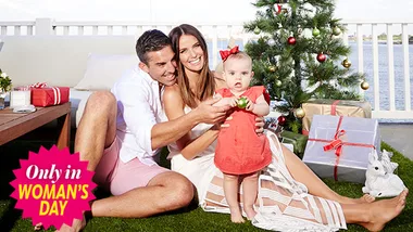 Family celebrating Christmas outdoors, with a decorated tree and gifts, smiling and dressed in summer attire.