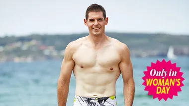 Man standing shirtless on beach with ocean background, "Only in Woman's Day" badge on image.
