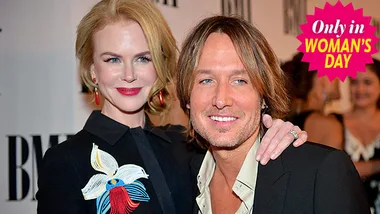 Two individuals smiling at an event, with one embracing the other, both dressed elegantly.