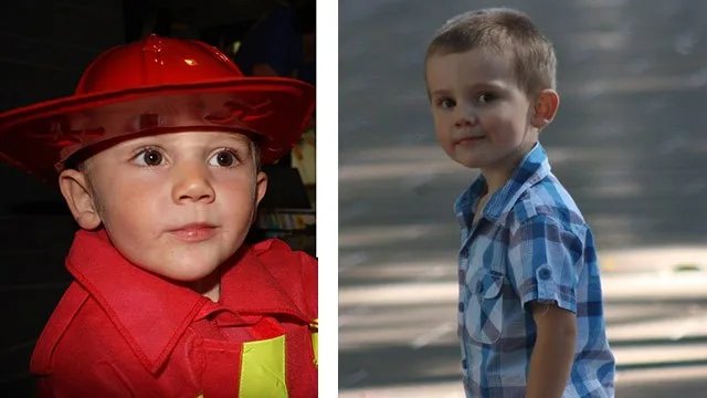 Young child in red firefighter costume and blue plaid shirt outdoors.