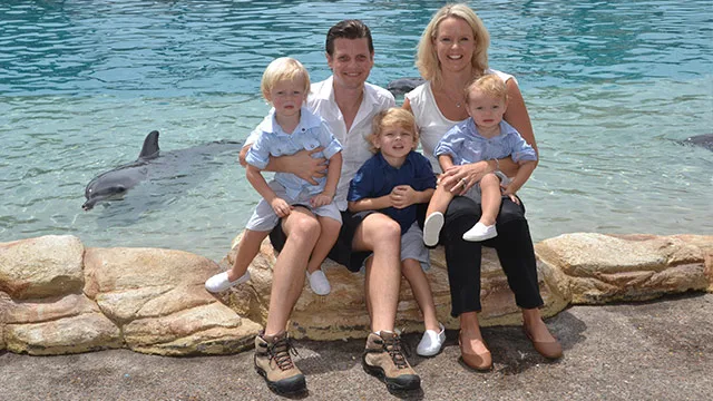 A family with three children sitting by a dolphin pool, smiling for the camera.