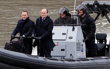 Daniel Craig, as James Bond, rides a speedboat on the Thames with crew members, filming a scene for a 007 movie.