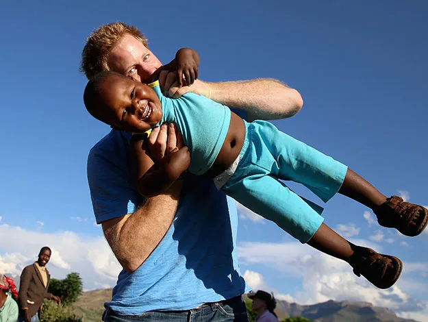 Man playfully swings a joyful child in the air under a clear blue sky.