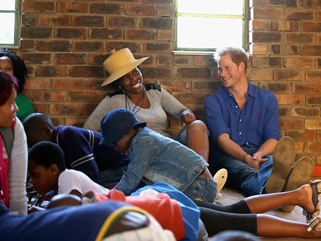 A group of people sitting together on the floor, with a man smiling and others engaged in conversation, against a brick wall.