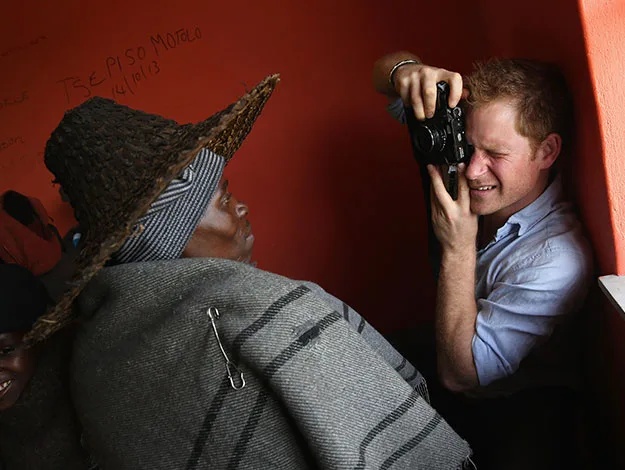 Man with camera photographs person in traditional attire and woven hat against orange wall.