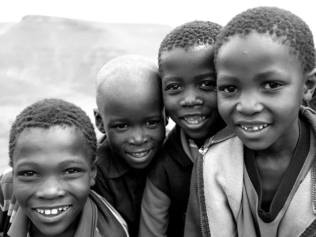 Four smiling children in black and white photo, standing closely together outdoors.