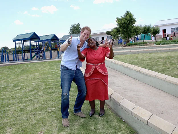 Man and woman smiling, posing playfully in a park with playground in background, sunny day.