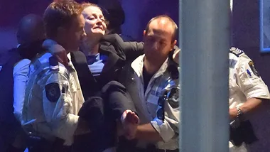 A woman being carried by police officers during a hostage situation response.