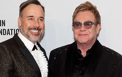 Two men in formal attire smiling at a formal event backdrop.