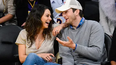 A couple sitting courtside at a basketball game, smiling and chatting closely with each other.
