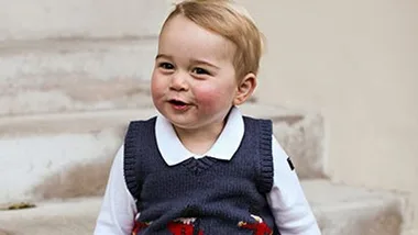 Young child sitting on steps wearing a festive sweater, smiling warmly with rosy cheeks.