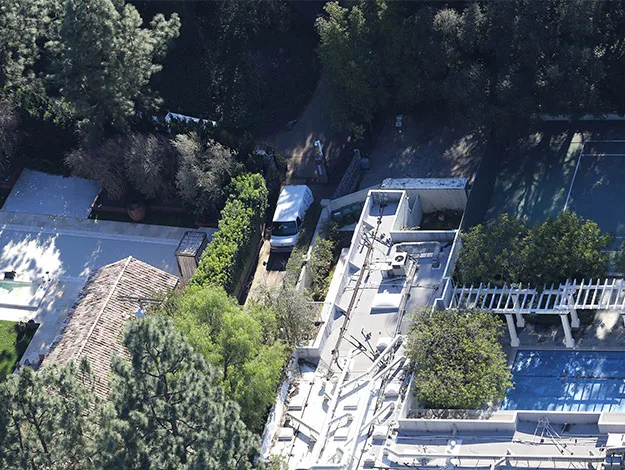 Aerial view of a residential property with trees, a white van, and a pool, surrounded by greenery.