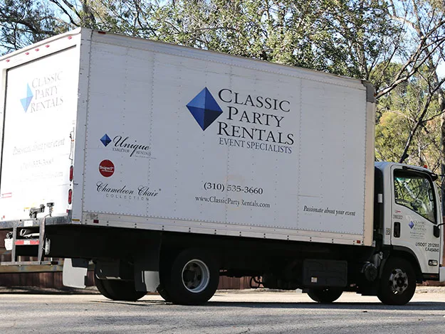 Delivery truck with "Classic Party Rentals" branding parked on a road, surrounded by trees.