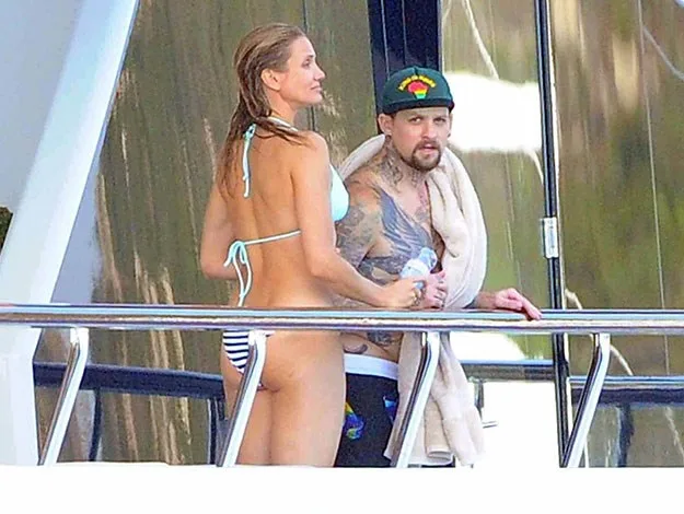 A man and woman in swimwear standing on a yacht deck, with the man holding a towel.