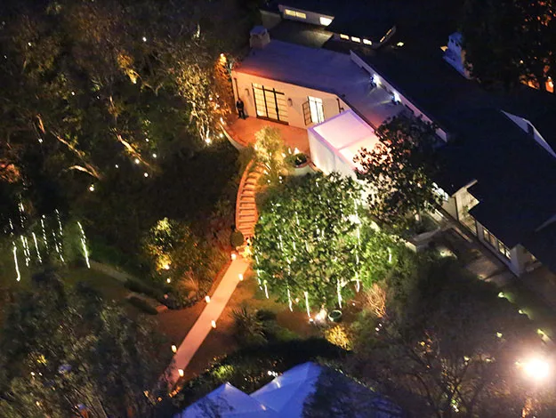 Aerial view of a well-lit house and garden with a winding path at night.