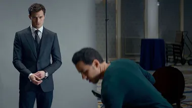 A suited man stands solemnly beside another bending man, set in an interior space with muted colors.