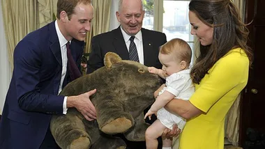 Man holding a large stuffed animal while a woman and a baby in white observe, with an elderly man in the background.