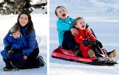 Mother and young child seated on snow; two children sledding joyfully nearby.
