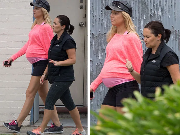 Two women walking, one pregnant in a pink top and black shorts, the other in black activewear. Both look ahead focused.
