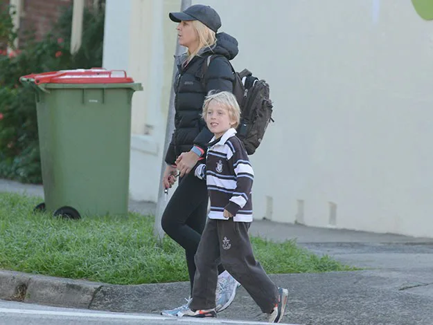 A woman and young boy walk on a sidewalk together; she is in a black jacket and cap, while he wears a striped sweater.