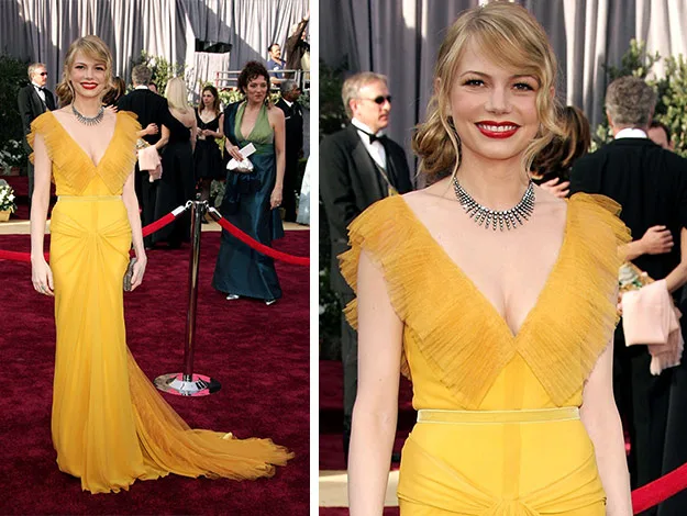 Woman in a yellow gown with a deep V-neck and a statement necklace on the red carpet at an event.