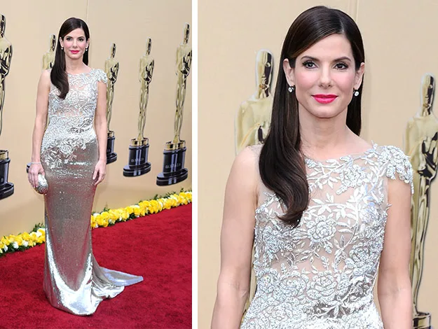 Woman in an elegant silver gown on the red carpet, Oscars backdrop with statue silhouettes in the background.