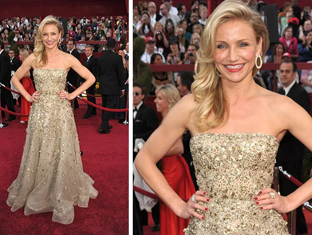 Blonde woman in a gold strapless gown poses on a red carpet event, smiling and hands on hips, surrounded by attendees.