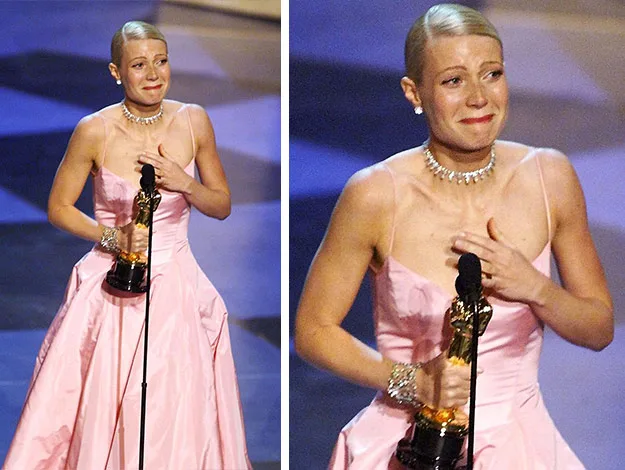Oscar winner in pink dress with trophy, teary-eyed on stage, hand on chest.