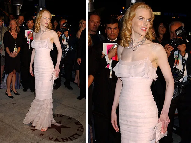A woman in a pink ruffled gown poses on a red carpet event, surrounded by photographers and onlookers.