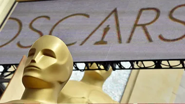 Oscar statuettes in front of a blurred Oscars sign background.