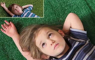 A child lies on green grass, arms behind head, mimicking a scene from "Boyhood" depicted in an inset image above.