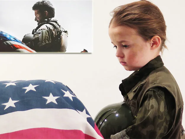 Child in military attire holding helmet, beside a flag-draped coffin, with a soldier&rsquo;s image in the background.