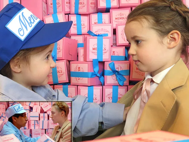 Two children dressed as characters from "The Grand Budapest Hotel" in front of pink Mendls boxes; inset with movie scene.