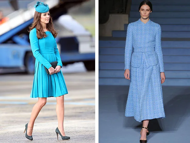 "Two women in blue outfits; left in a teal dress and hat, right in a long light blue coat on runway."