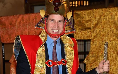 Prince William wearing traditional Japanese attire and smiling, holding a sword during a cultural event in Japan.