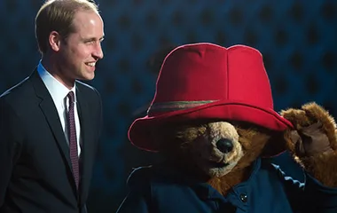 Prince meets Paddington Bear in red hat and coat, both smiling at an event.