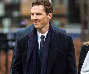 A person in a suit standing outdoors with a slight smile on a rainy day.