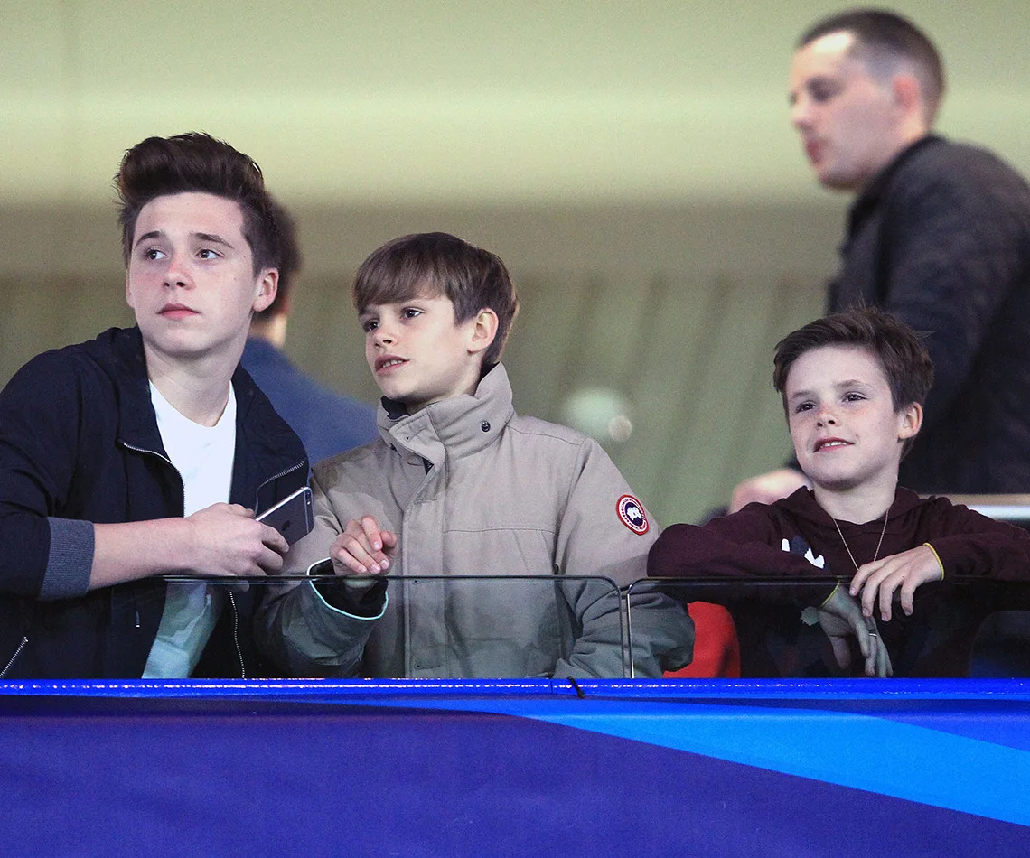 Three boys watching an event from a balcony, wearing casual jackets, with expressions of interest and enjoyment.