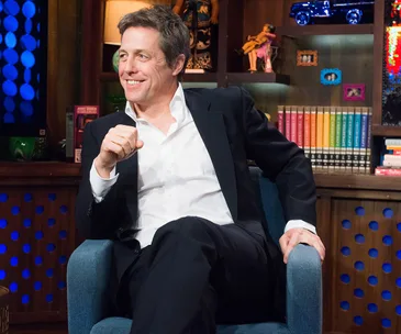 Actor sits in a talk show setting, smiling, wearing a dark suit and white shirt.