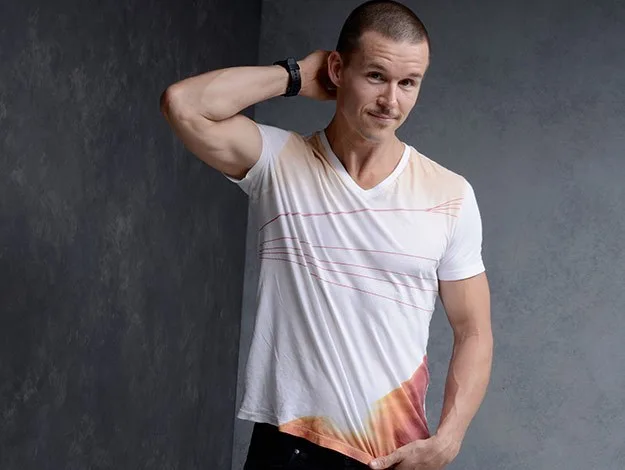 Man in a white graphic tee with short hair poses against a gray background.