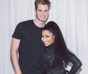 A tall man with light hair and a smiling woman with long black hair pose together in front of a white curtain.